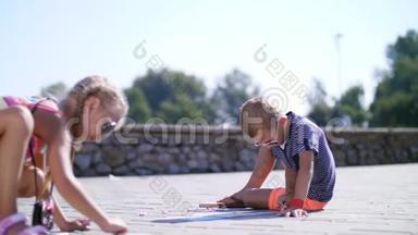 孩子们，一个男孩和一个女孩戴着太阳镜，用彩色蜡笔在沥青上画画，街道瓷砖。 <strong>炎炎夏日</strong>..